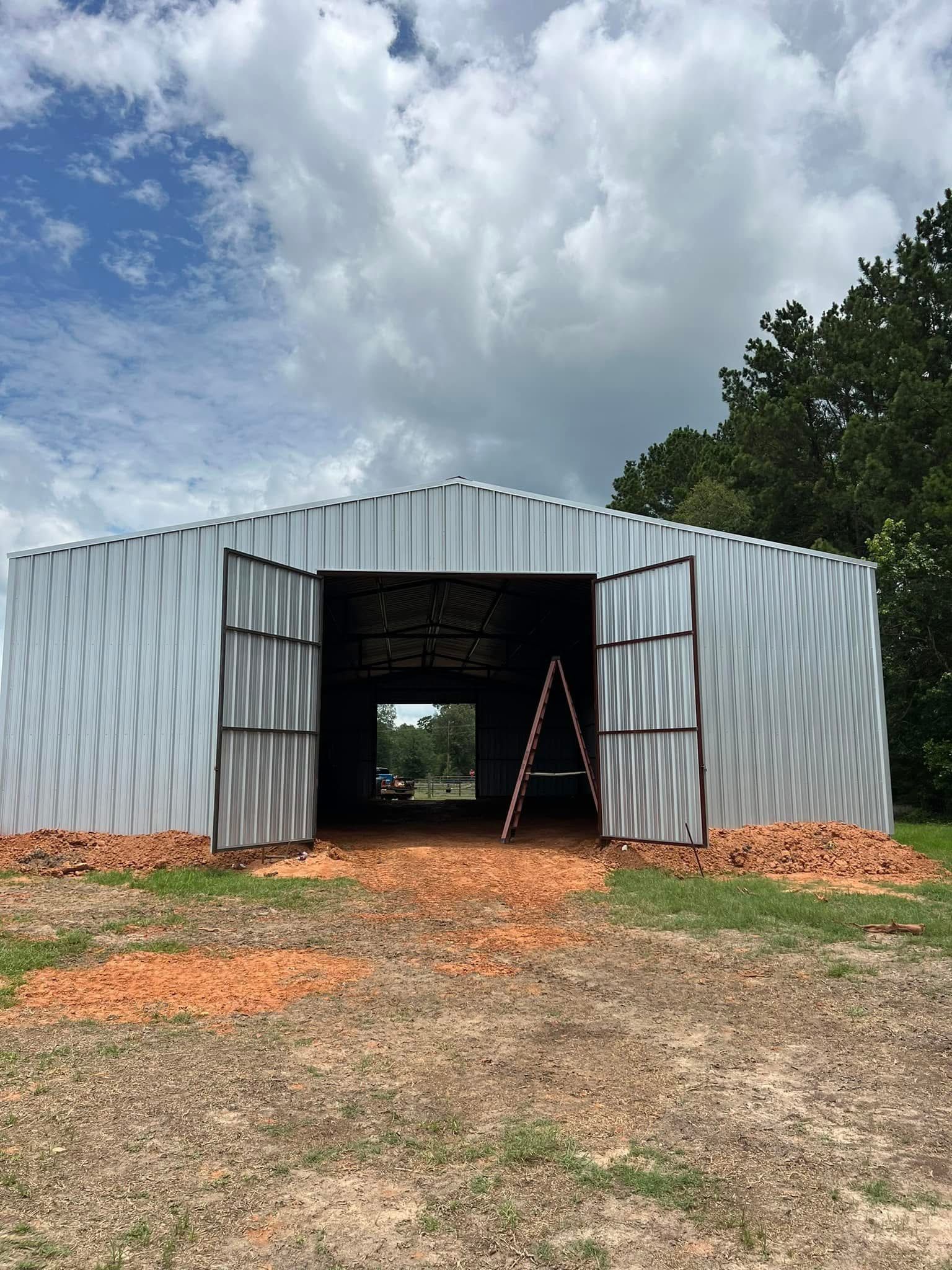 Metal barn with open doors, ladder inside, on a grassy field, under a cloudy sky.