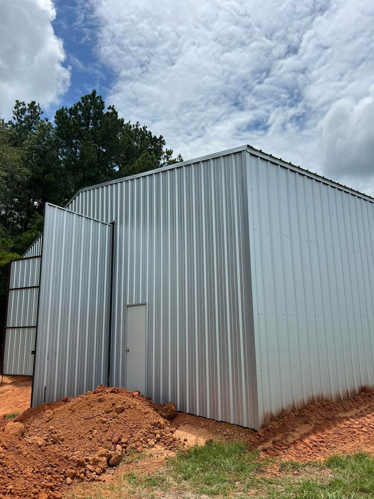 Metal-sided building under cloudy sky; dirt pile in front.