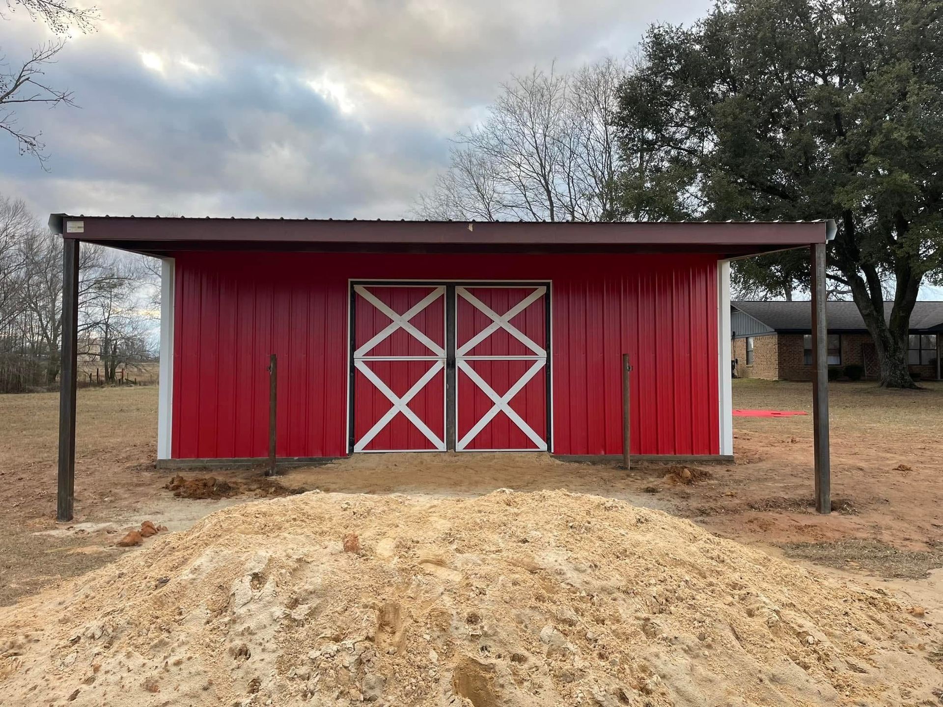 Red barn with brown roof and white cross doors; dirt pile in front.