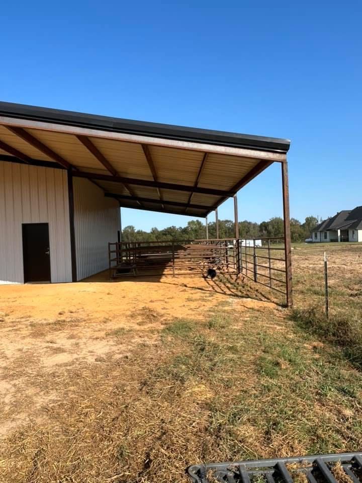 Metal barn with brown roof and stalls, on a grassy field under a clear blue sky.