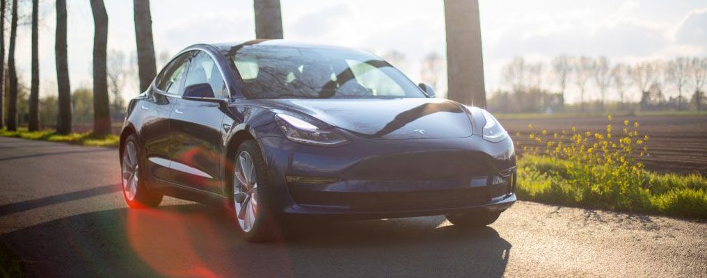 a tesla model 3 is parked on the side of a road .