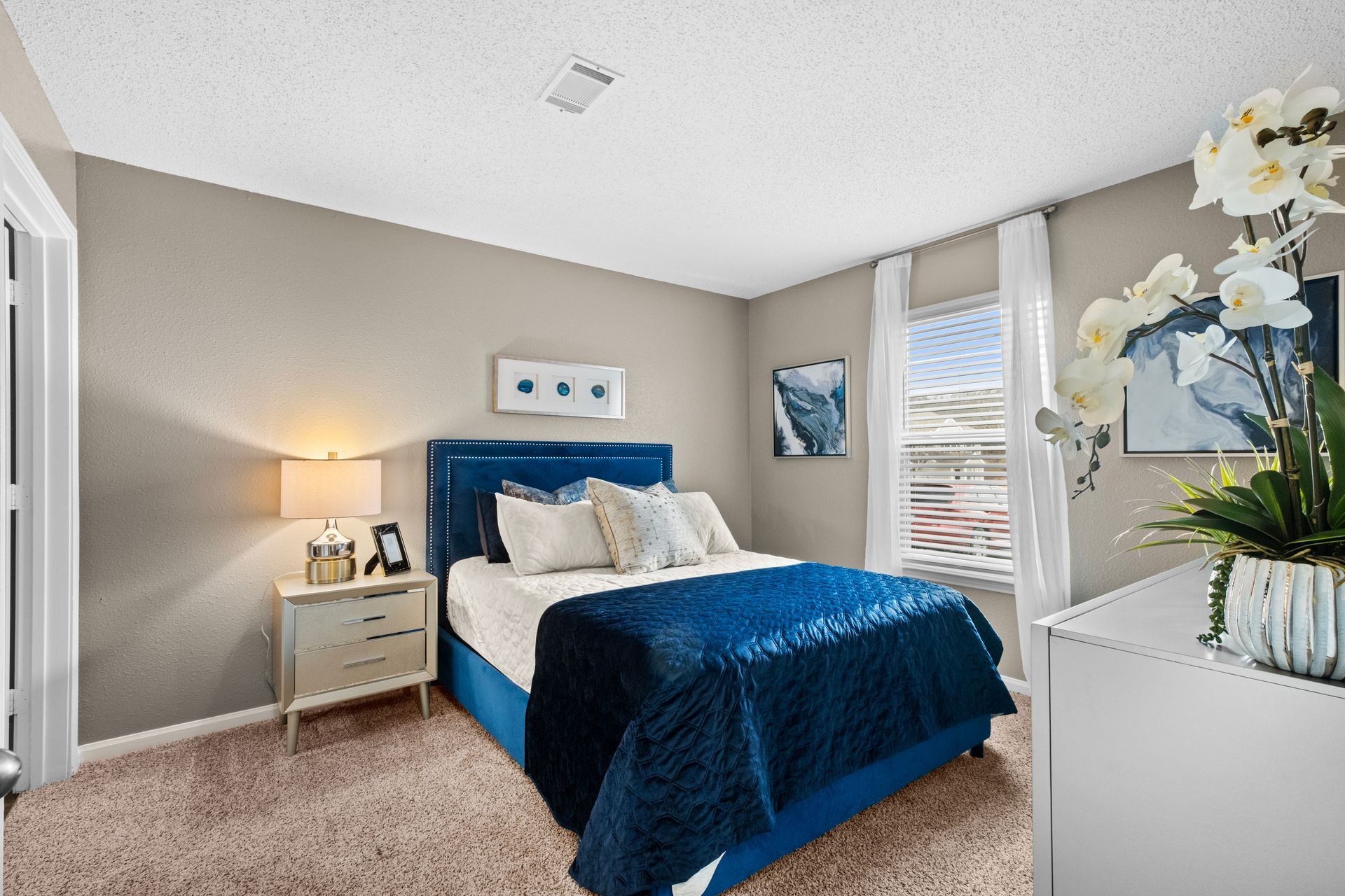 A bedroom with a bed , nightstand , dresser and window.