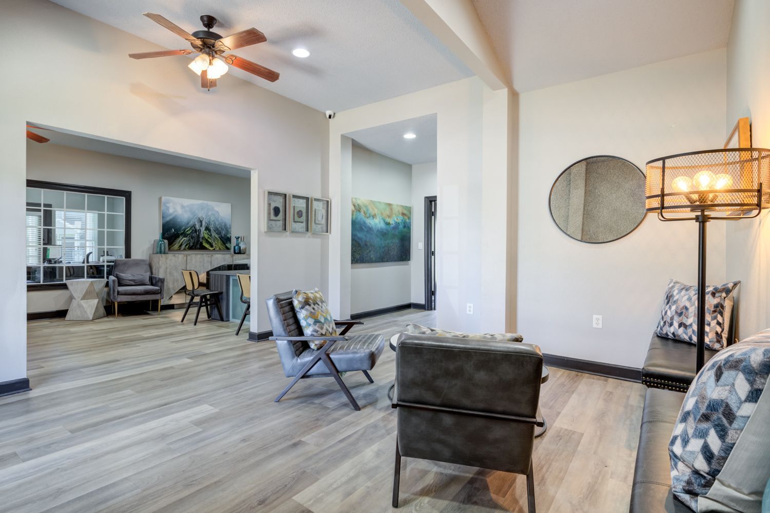Modern living room with chairs, bench, art, and a ceiling fan.