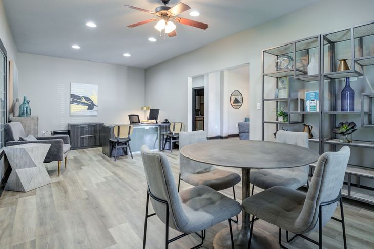 Modern office space with gray walls, round table and chairs, shelving unit, and desks.