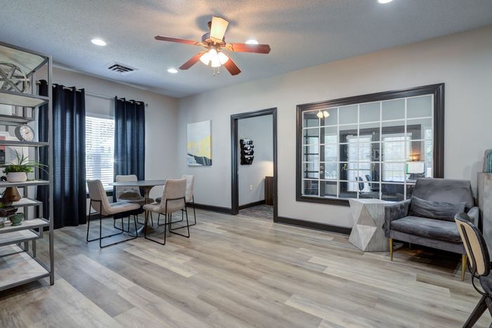 Living area with dining table, chairs, and seating area with gray armchair and geometric side table.