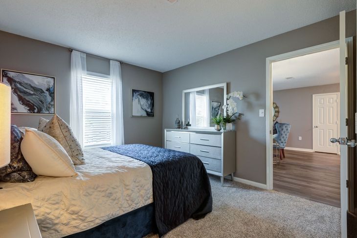 Bedroom with bed, dresser, art, window, and open door to another room. Gray walls, white trim, and carpet.