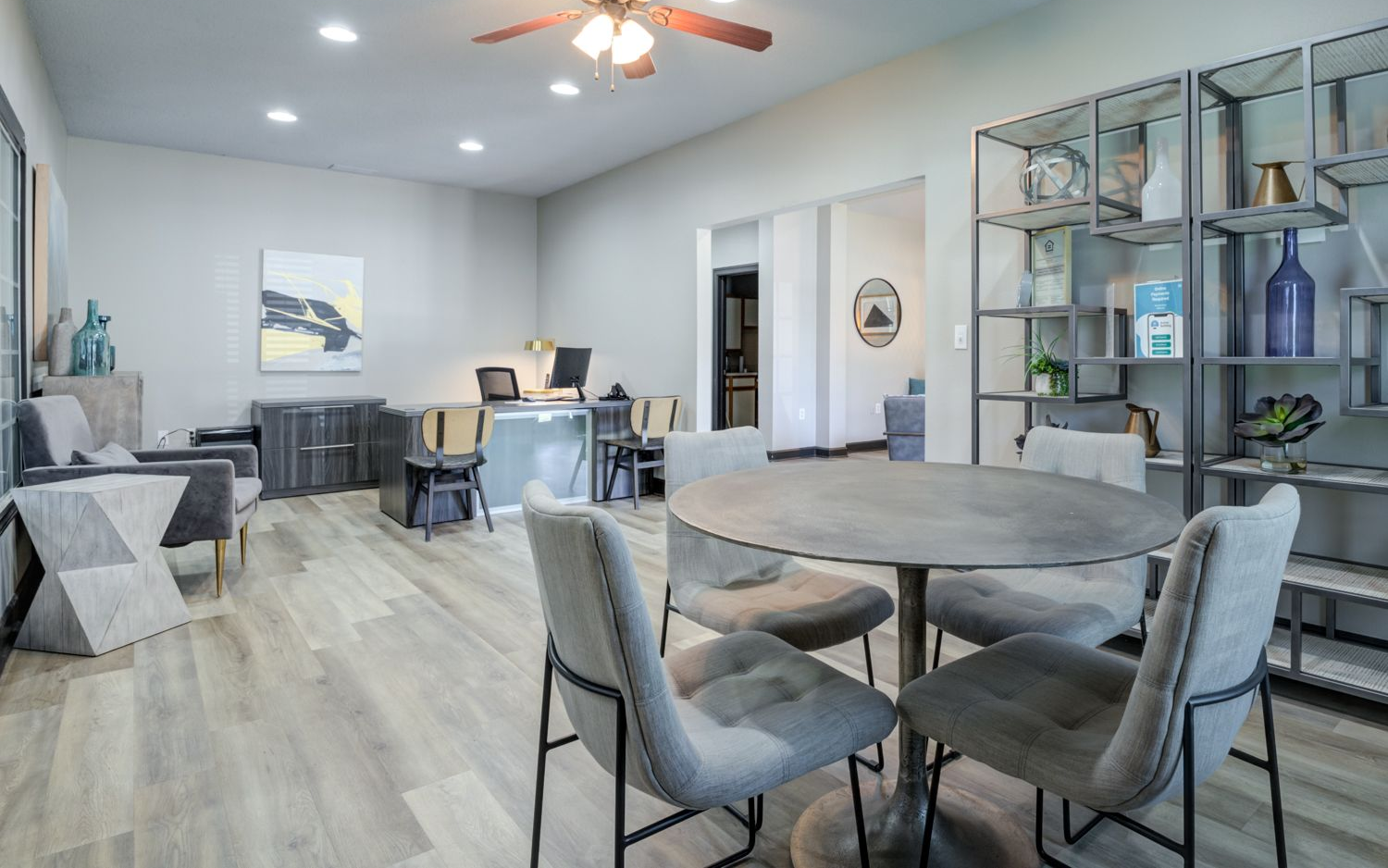 Modern office space with gray walls, round table and chairs, shelving unit, and desks.