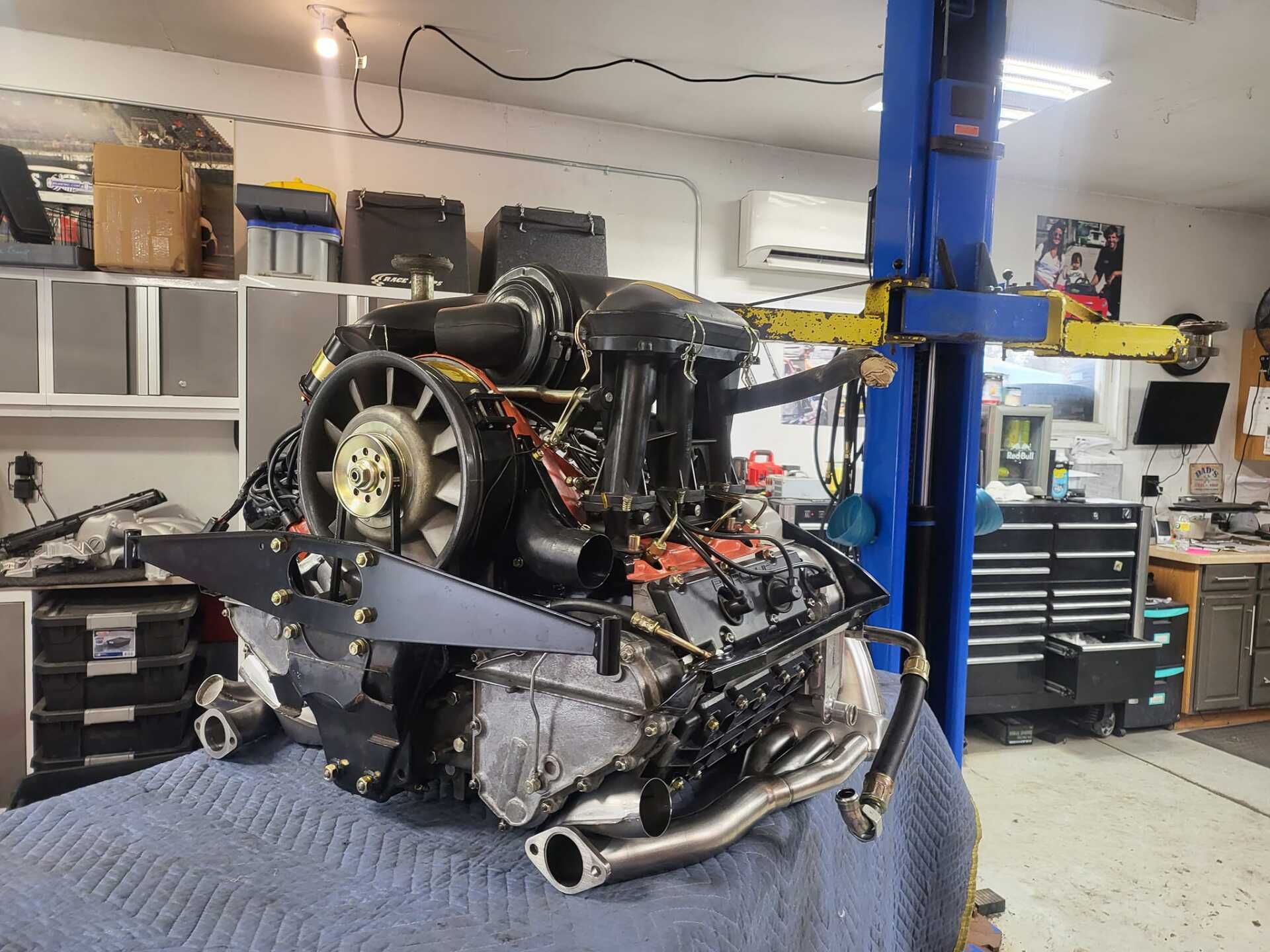 A Porsche engine on a blue sheet in a garage with tools and a lift.