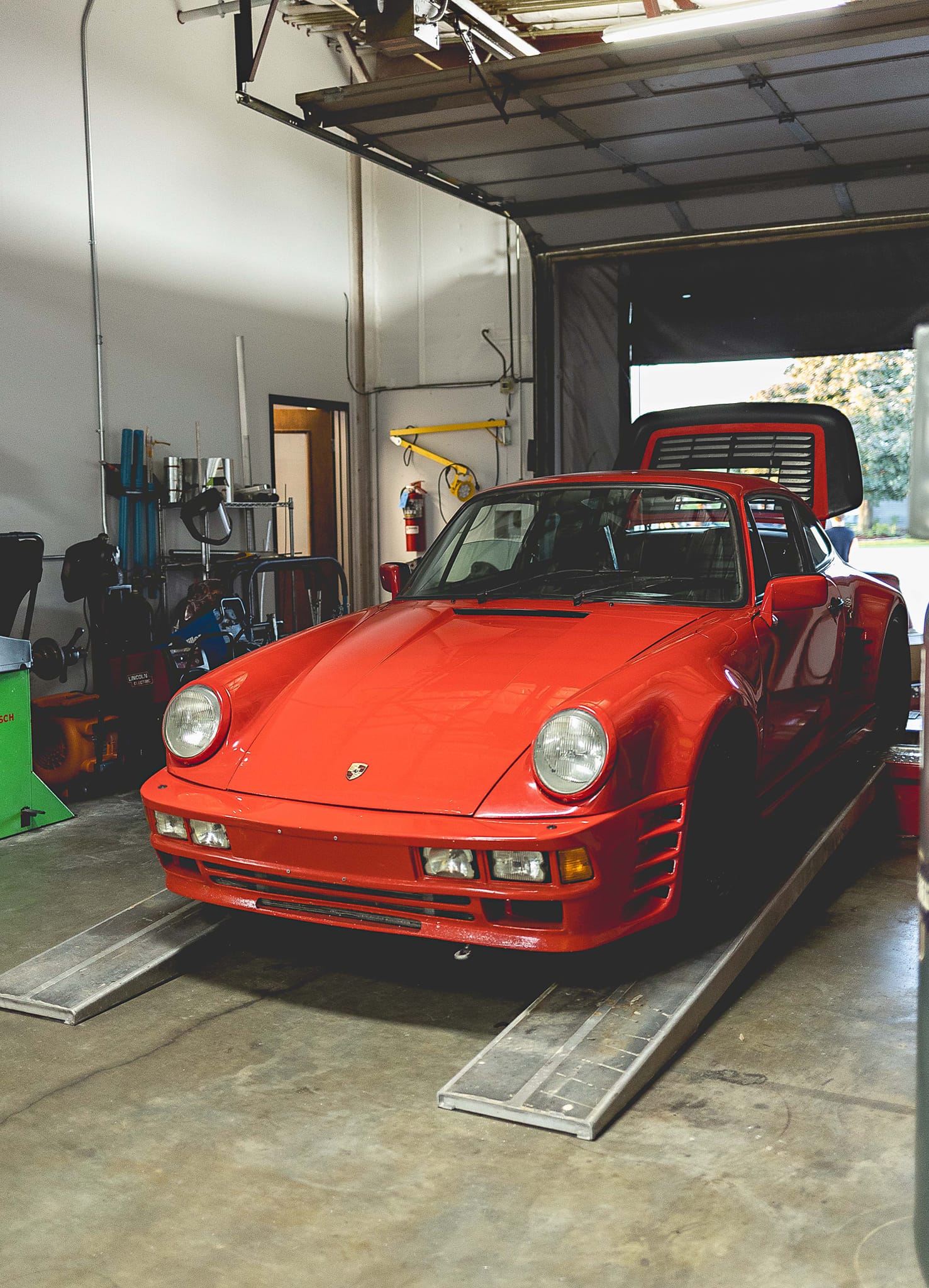 Red Porsche 959 sports car on ramps inside a garage.