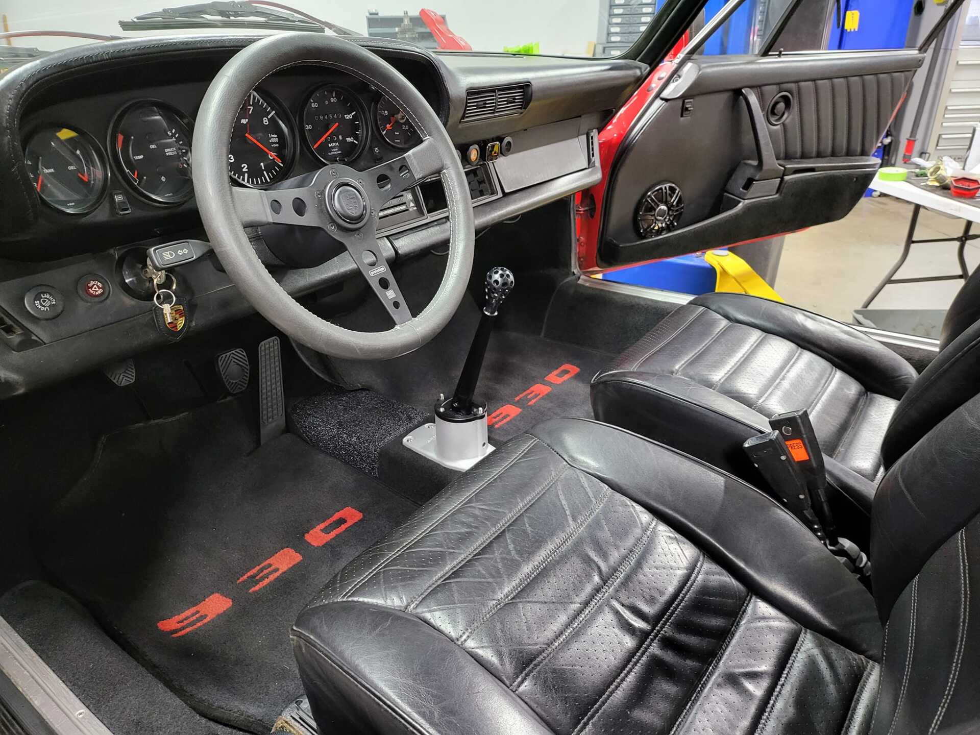 Interior view of a classic black and red Porsche 911, showing the dashboard, seats, and steering wheel.