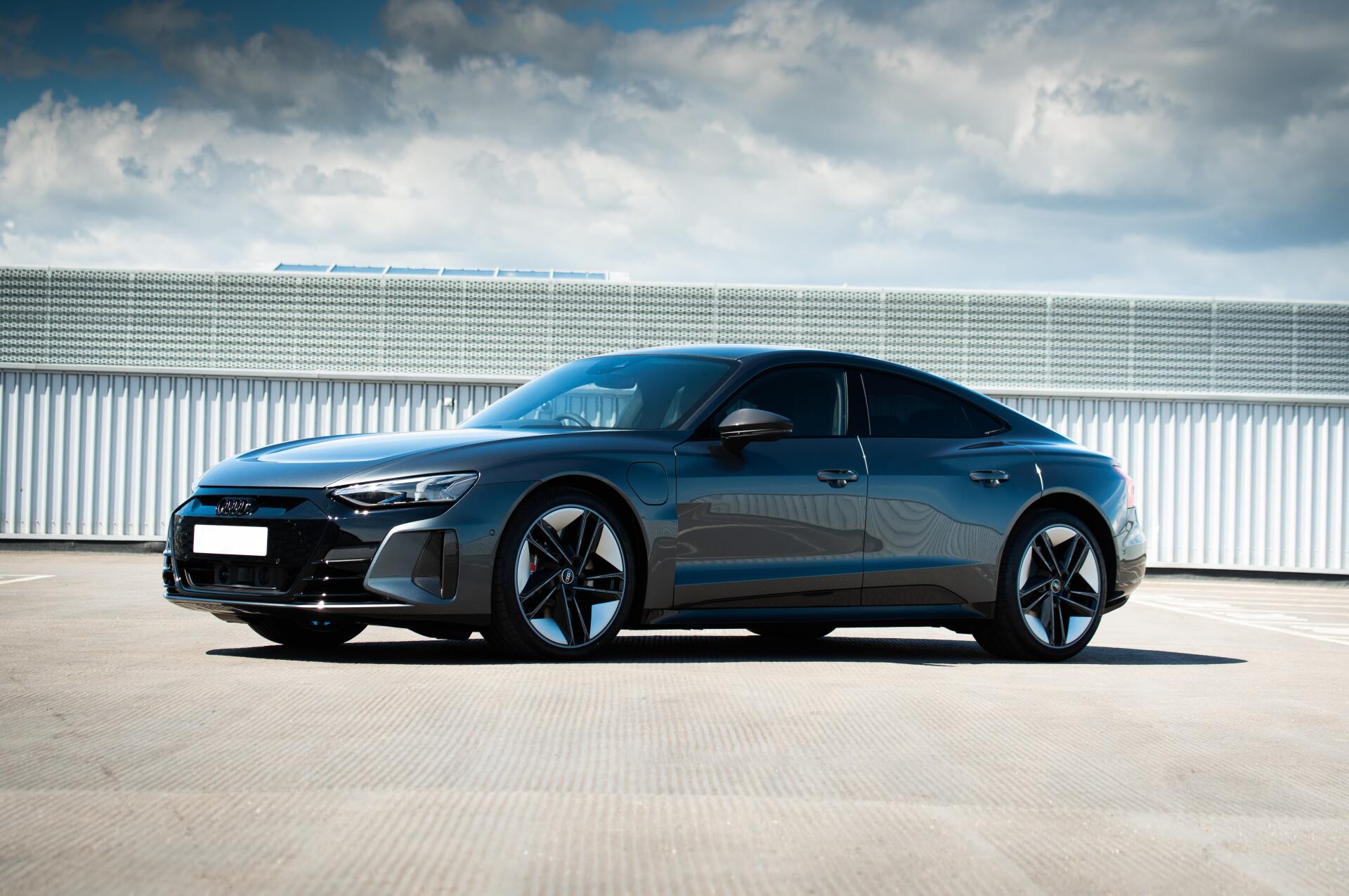 Gray Audi e-tron GT parked on a rooftop parking lot with a cloudy sky in the background.