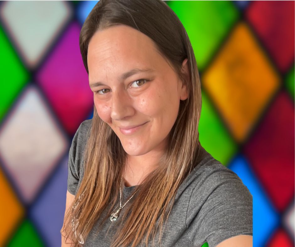 A woman wearing glasses is smiling in front of a stained glass window.