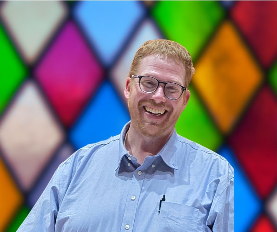A man wearing glasses is smiling in front of a stained glass window
