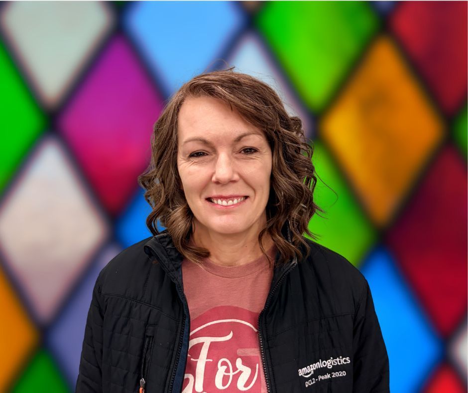 A woman wearing glasses is smiling in front of a stained glass window.