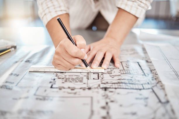 Architect providing design and drafting service with building blueprint and floor plan on desk.