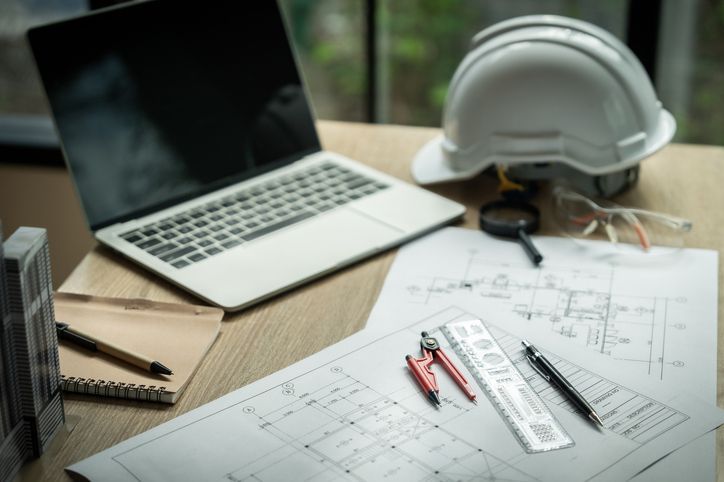 Architectural plans on a desk with a laptop, hard hat, and drafting tools. Architectural plans on a desk with a laptop, hard hat, and drafting tools.