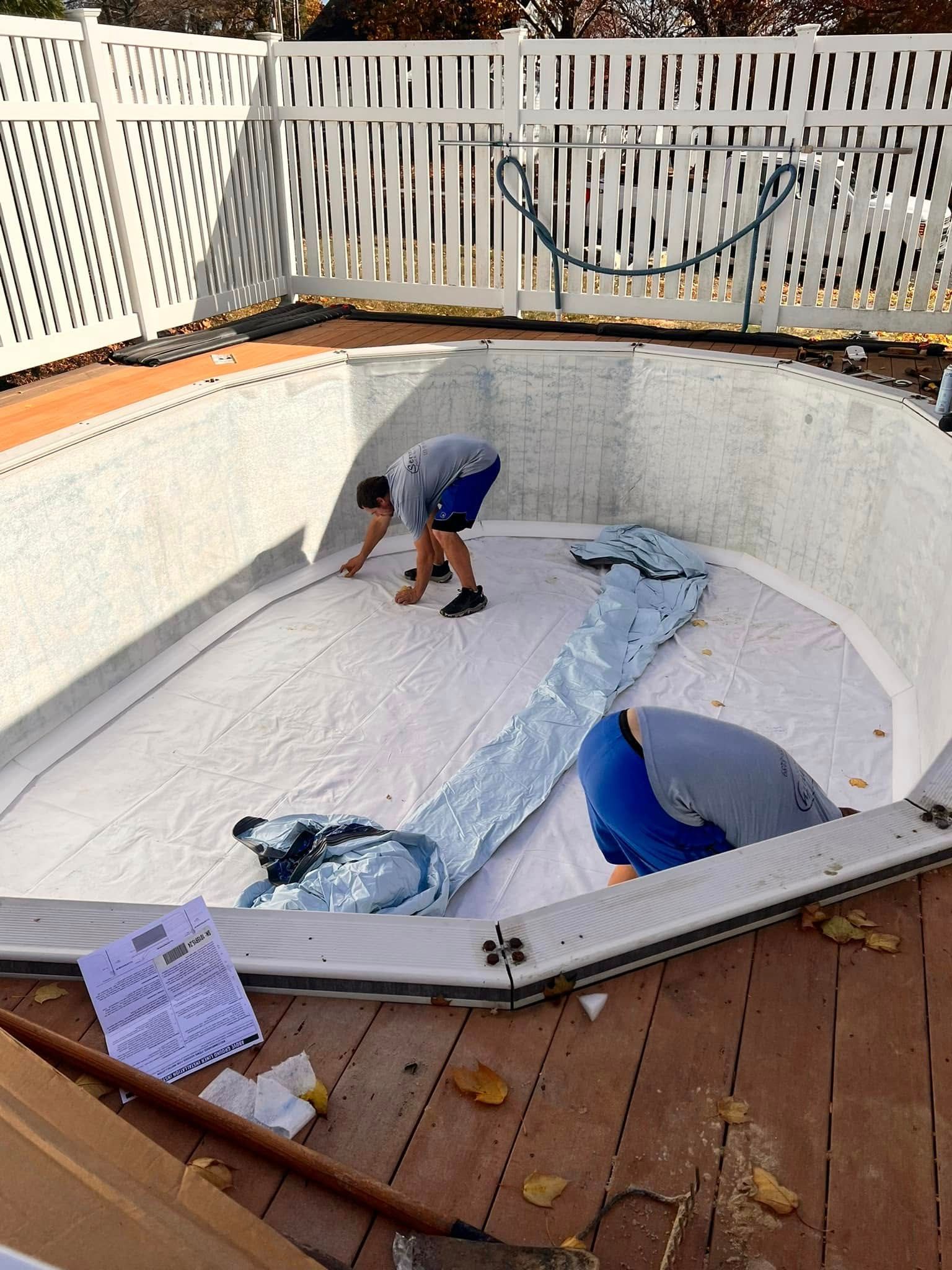 A man is working on a swimming pool with a white fence in the background.