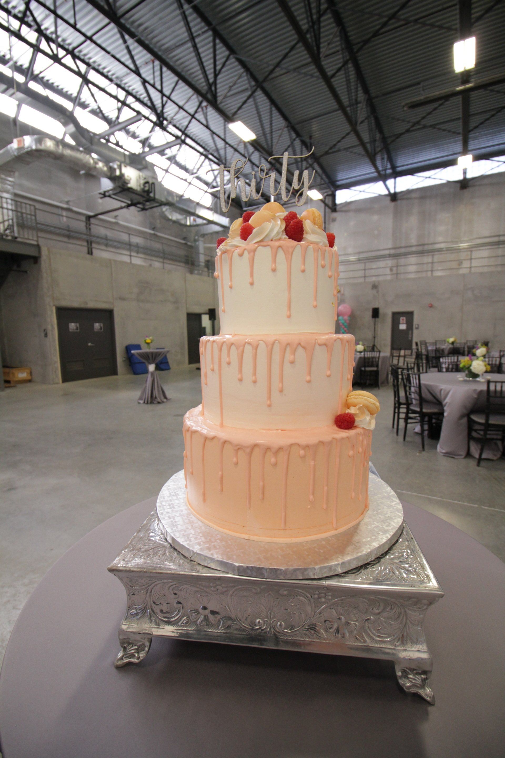 A three tiered cake is sitting on top of a silver cake stand.