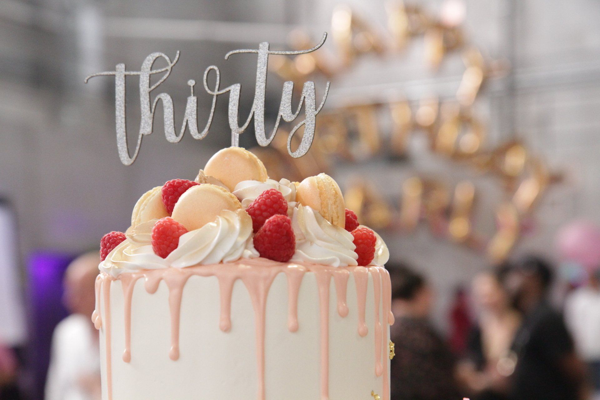 A birthday cake with raspberries and macarons on top of it.