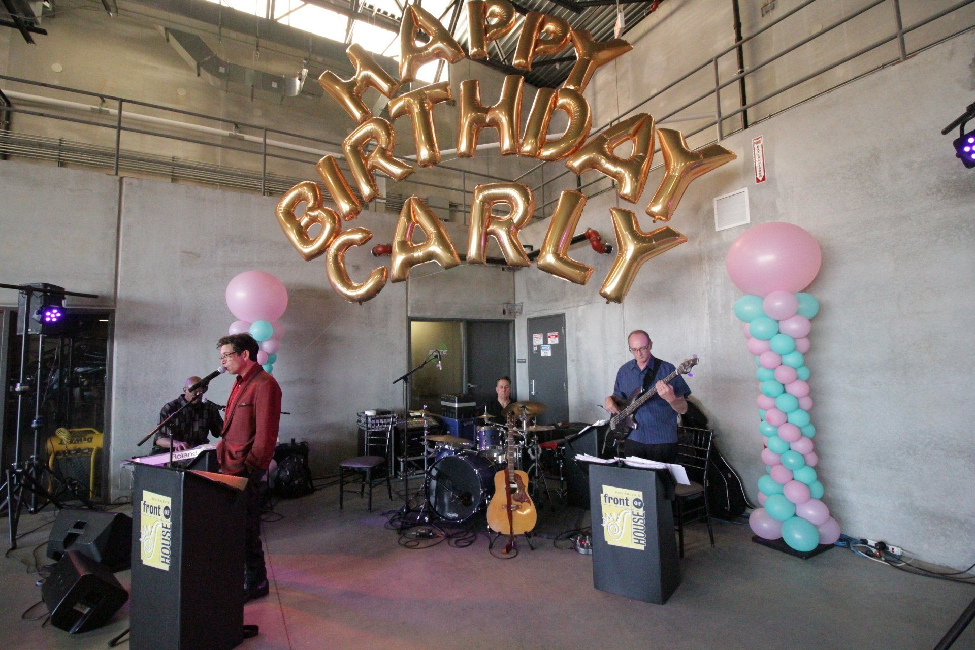 A group of people are playing instruments in front of balloons that say happy birthday carly