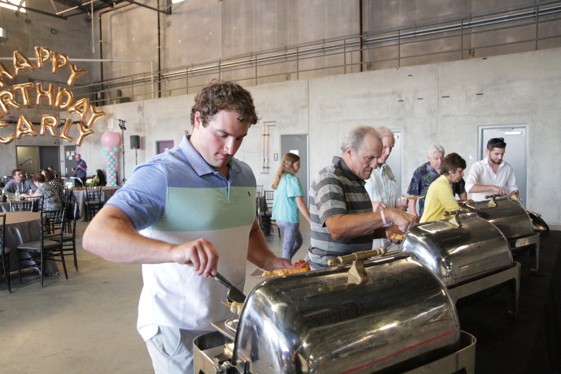 A man is standing in front of a buffet line at a birthday party.