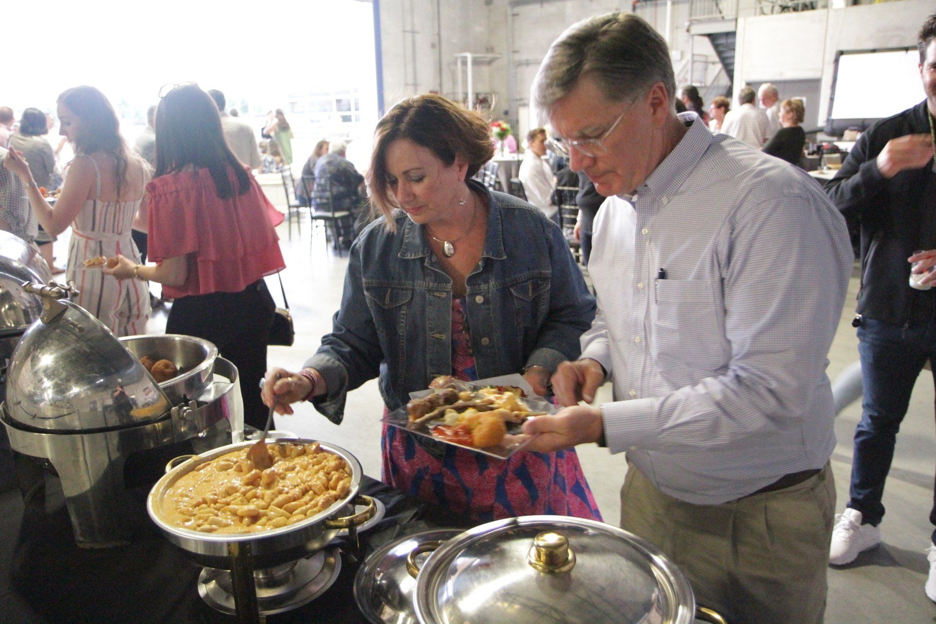 A man and a woman are getting food from a buffet table.