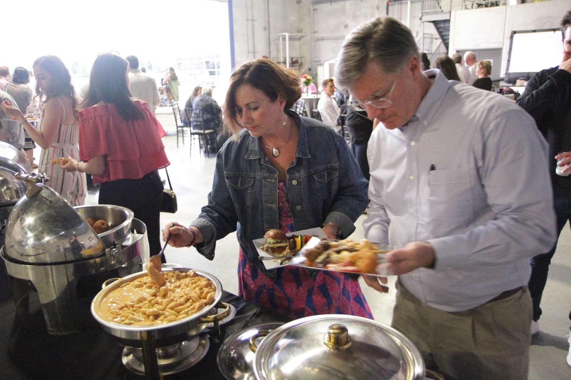 A man and a woman are standing at a buffet table eating food.