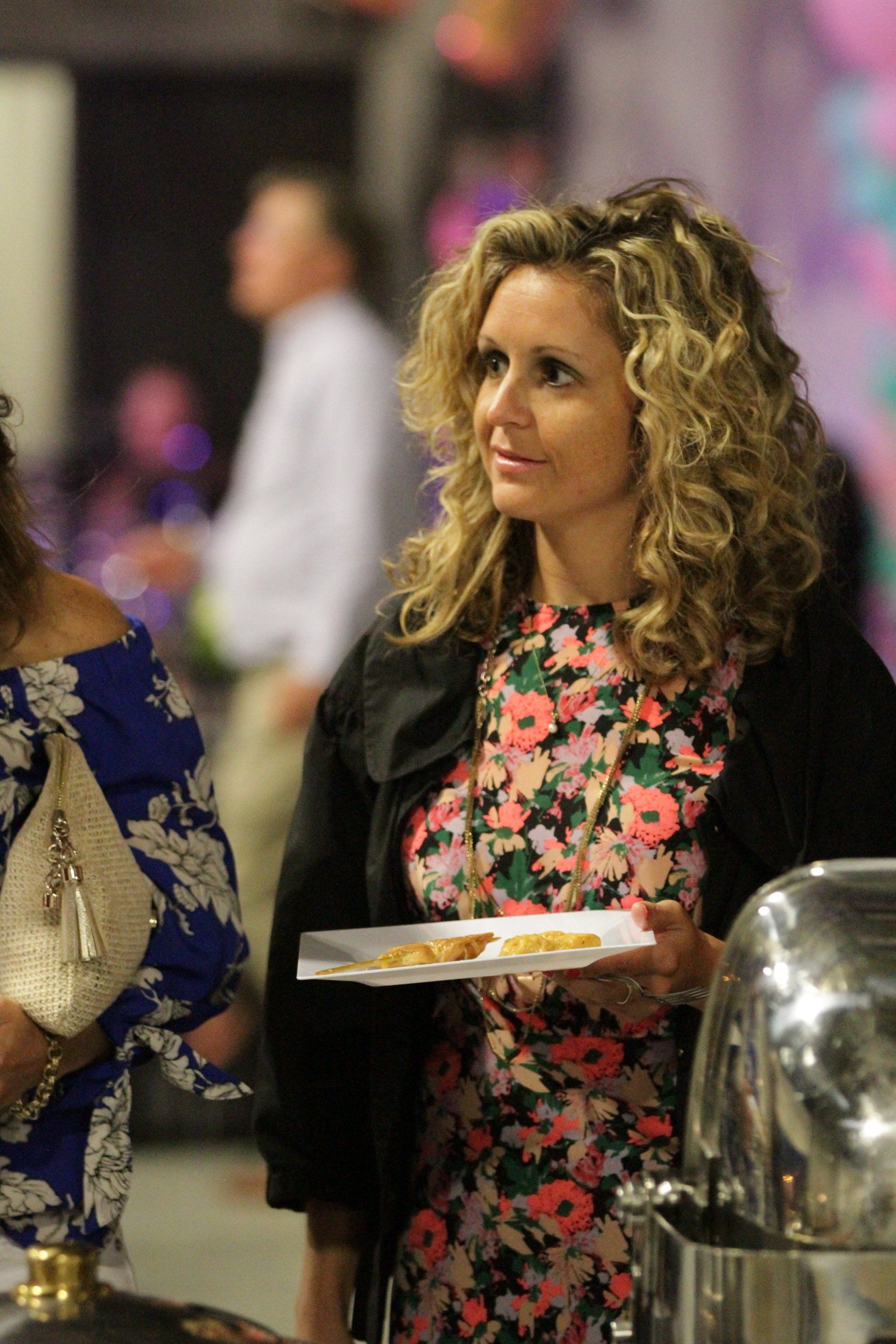 A woman in a floral dress is holding a plate of food.