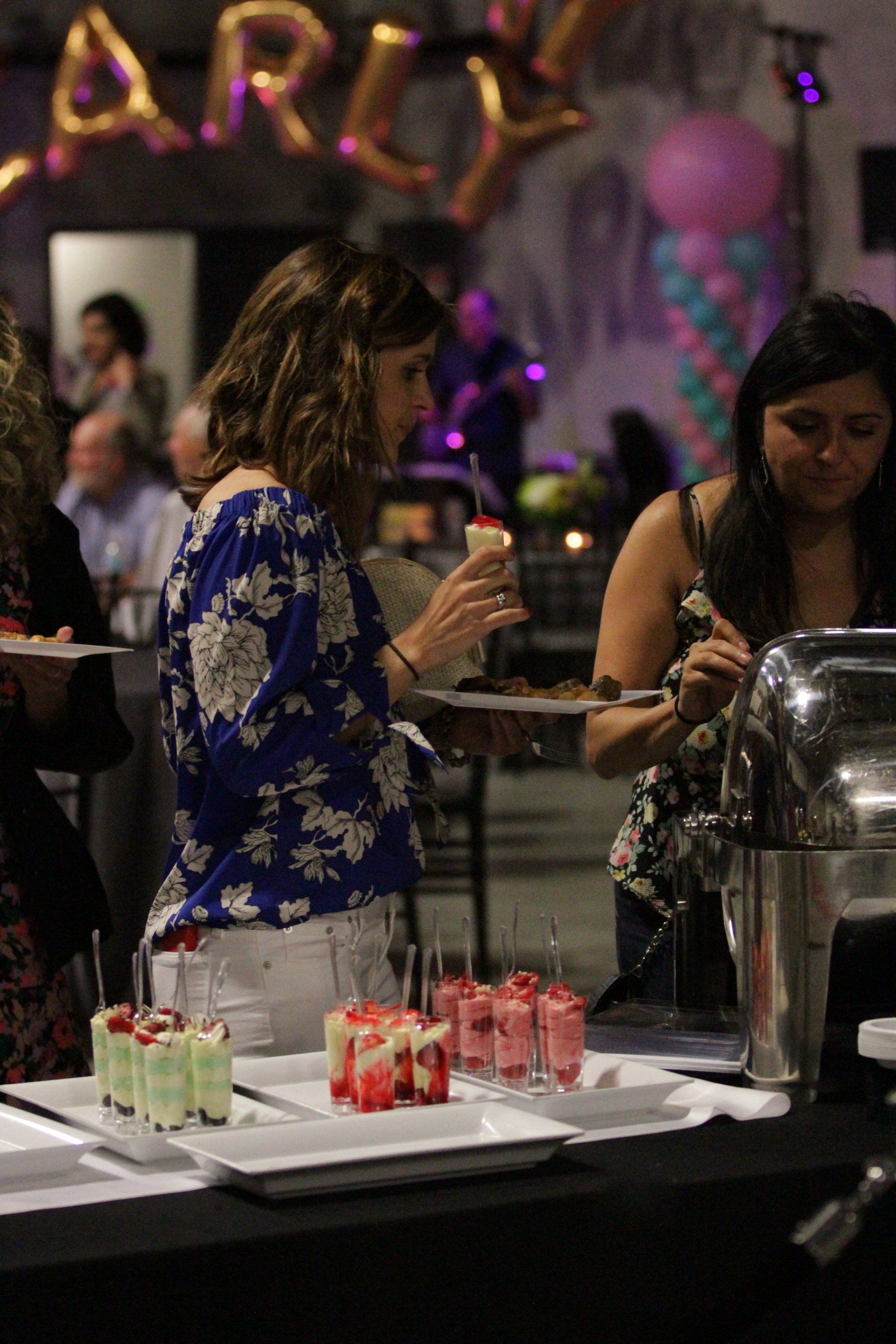 A group of women are standing around a table with plates of food.