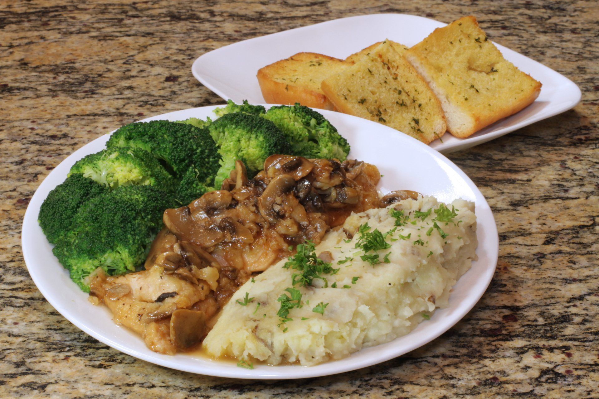 A plate of food with broccoli and mashed potatoes next to a plate of garlic bread