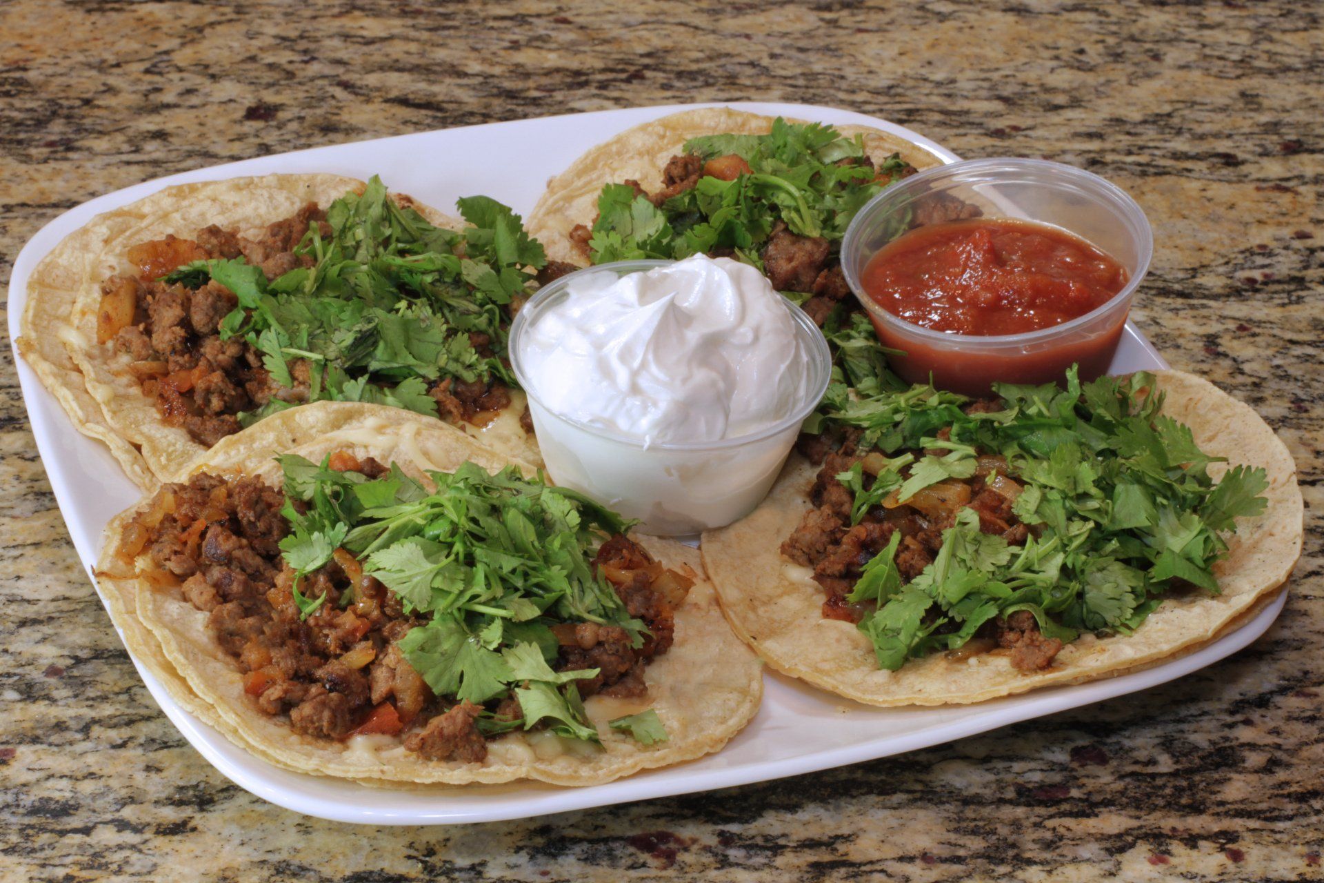 A plate of tacos with sour cream and salsa on a table.