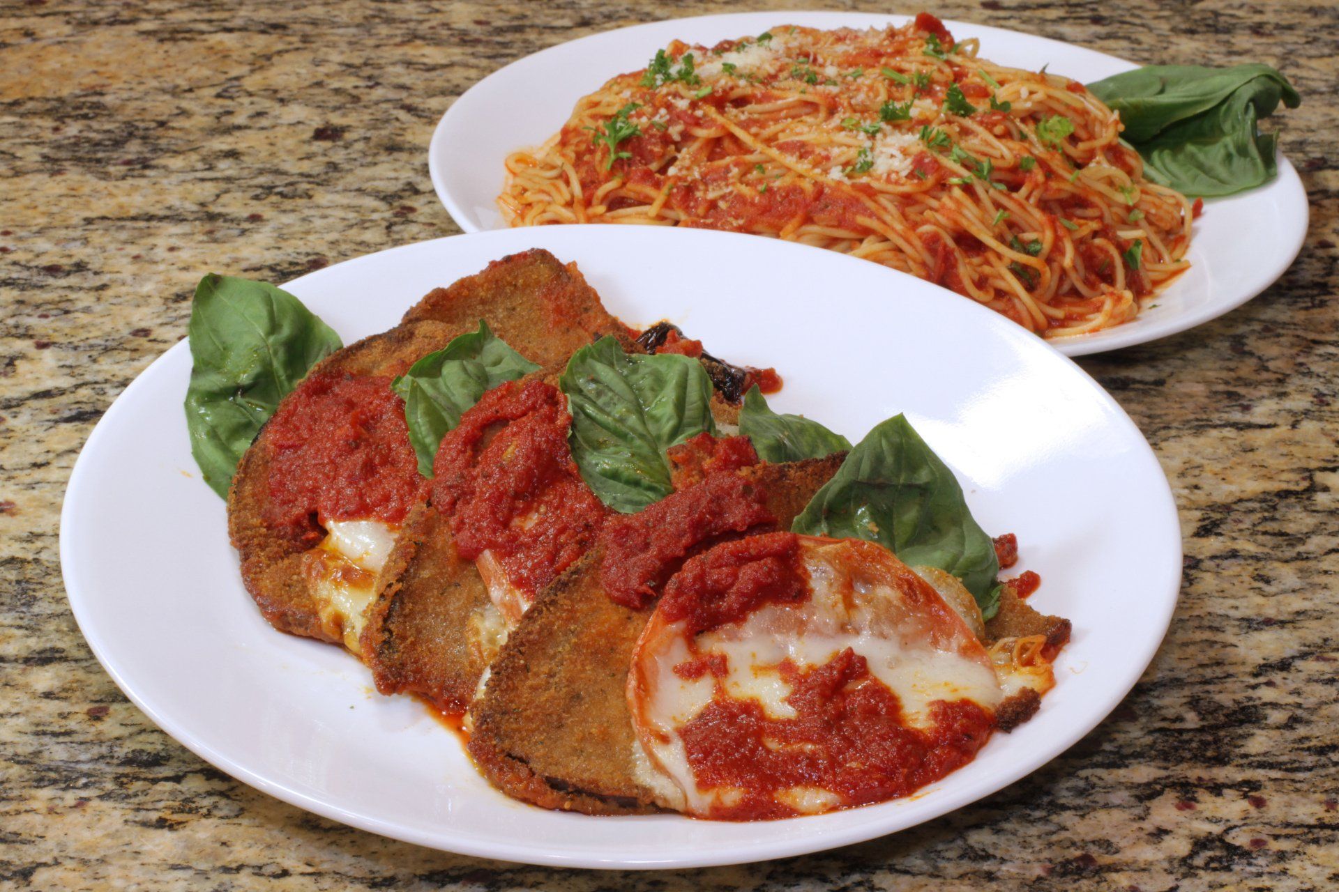 Two plates of food on a table , one of which is chicken parmesan.
