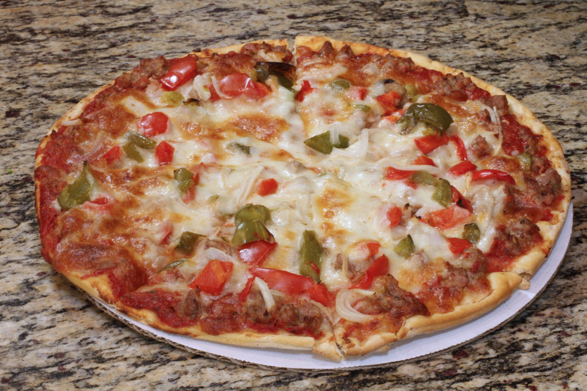 A pizza with tomatoes , peppers , onions and cheese on a white plate.