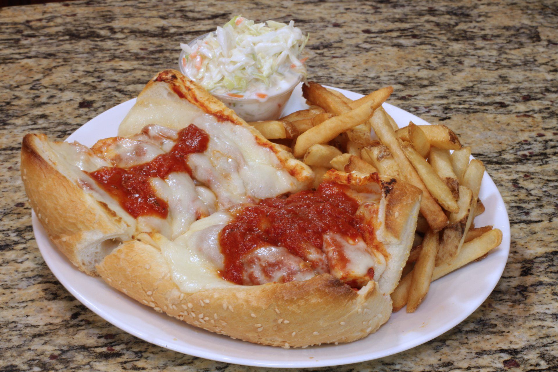 A pizza sub sandwich with french fries and coleslaw on a plate.