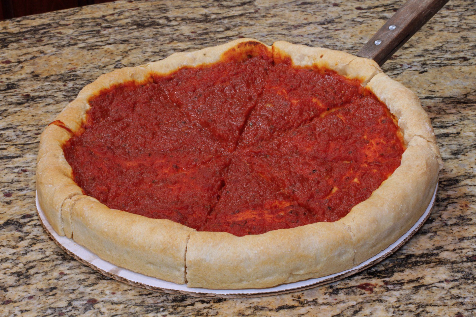 A pizza with tomato sauce on it is on a plate on a counter.
