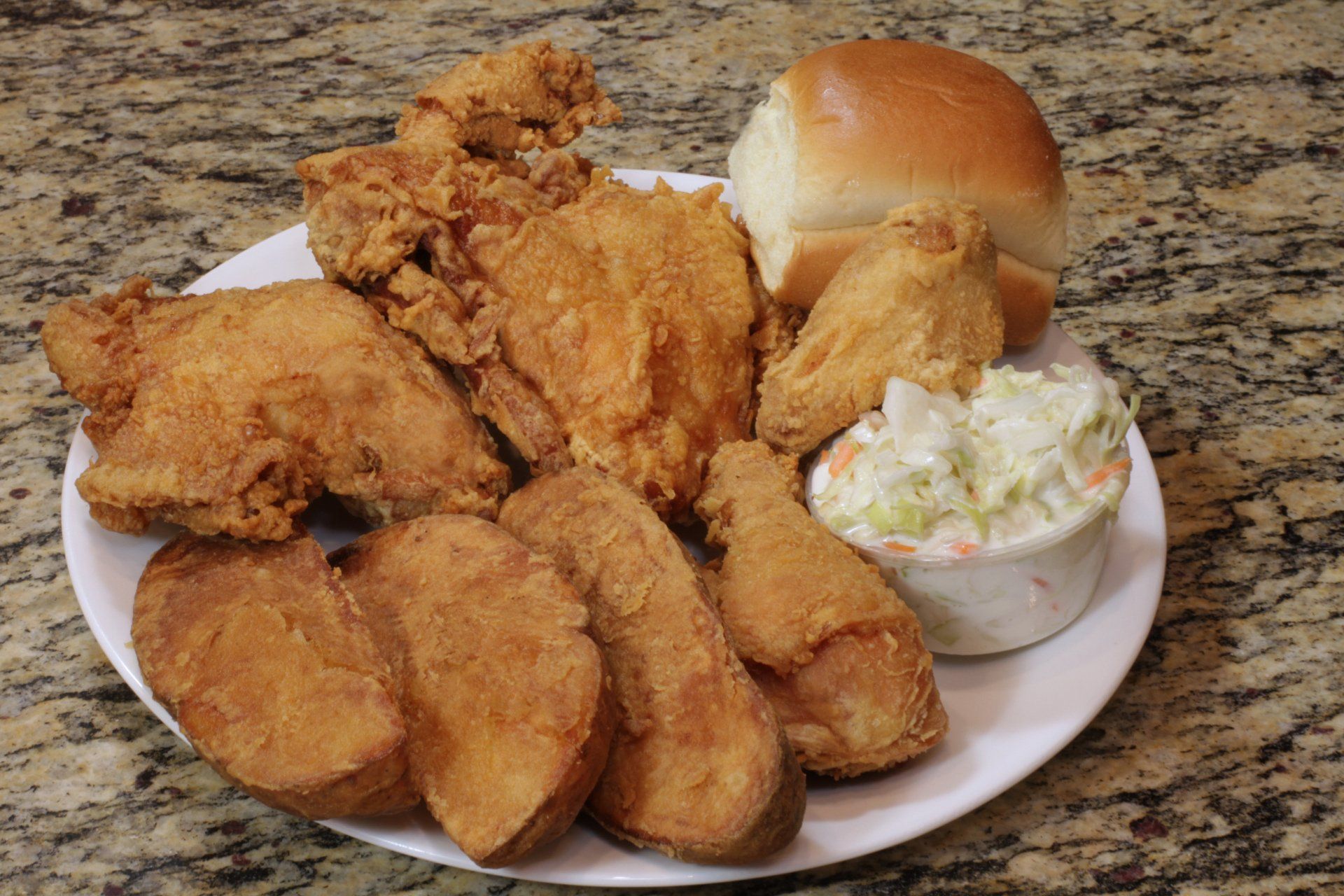 A white plate topped with fried chicken , potatoes , coleslaw and a roll.