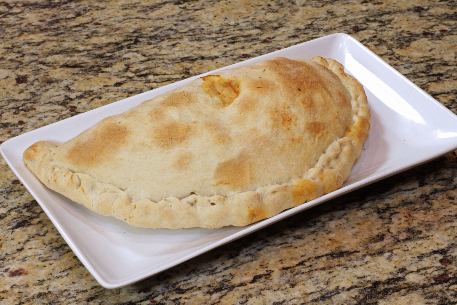A calzone is on a white plate on a granite counter top.