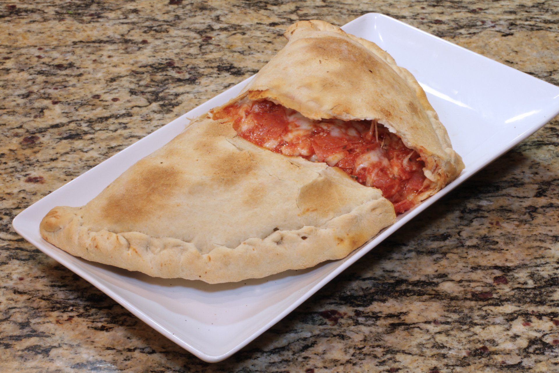 A half eaten pizza is on a white plate on a counter.