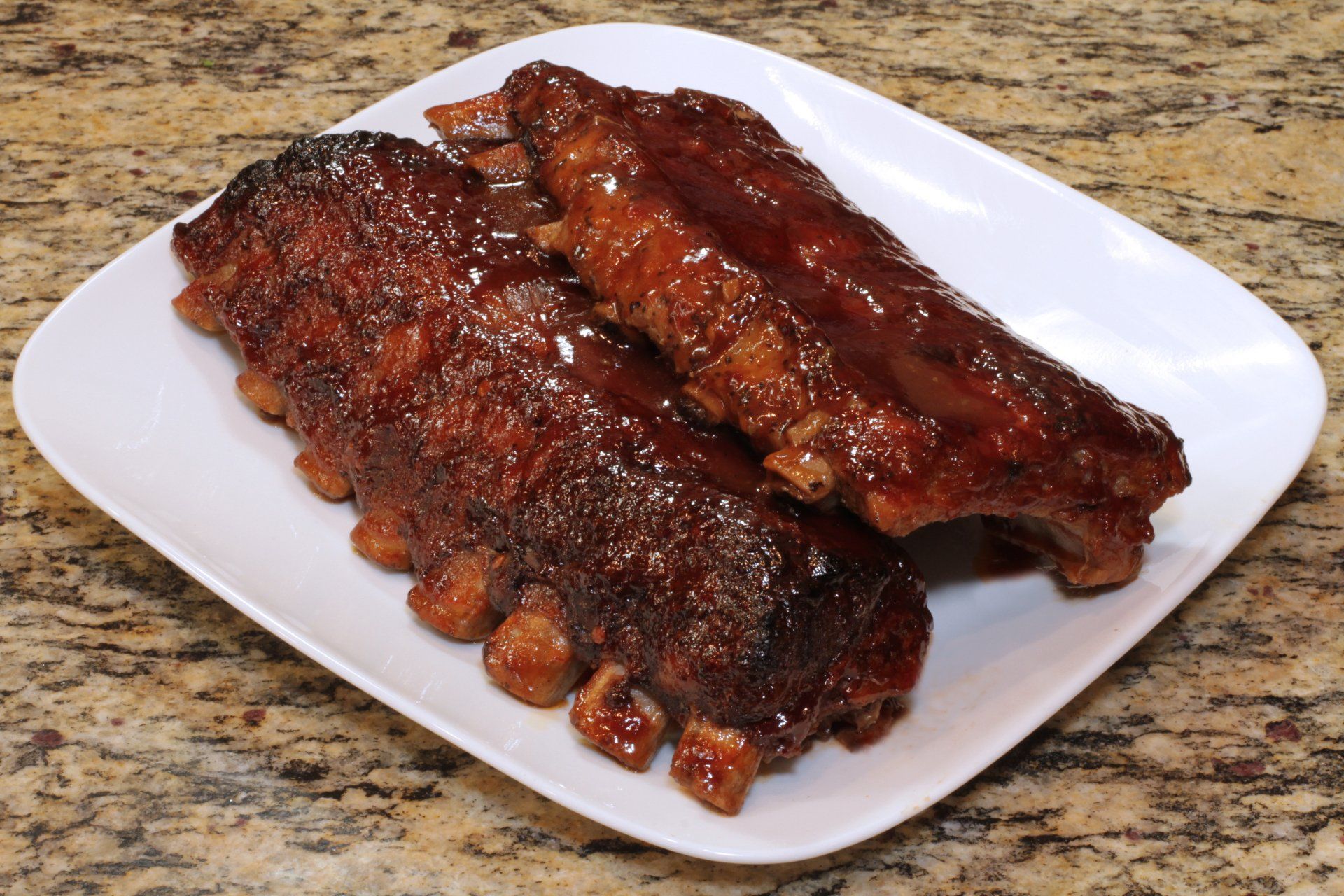 Two ribs on a white plate on a granite counter top
