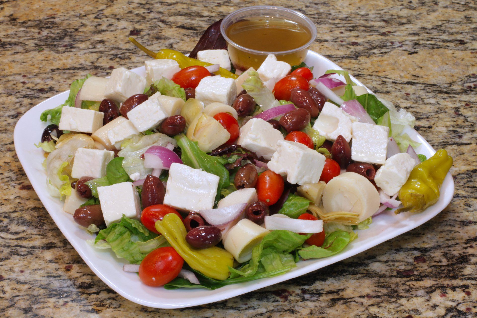 A salad with tomatoes , olives , feta cheese , onions and peppers on a white plate.