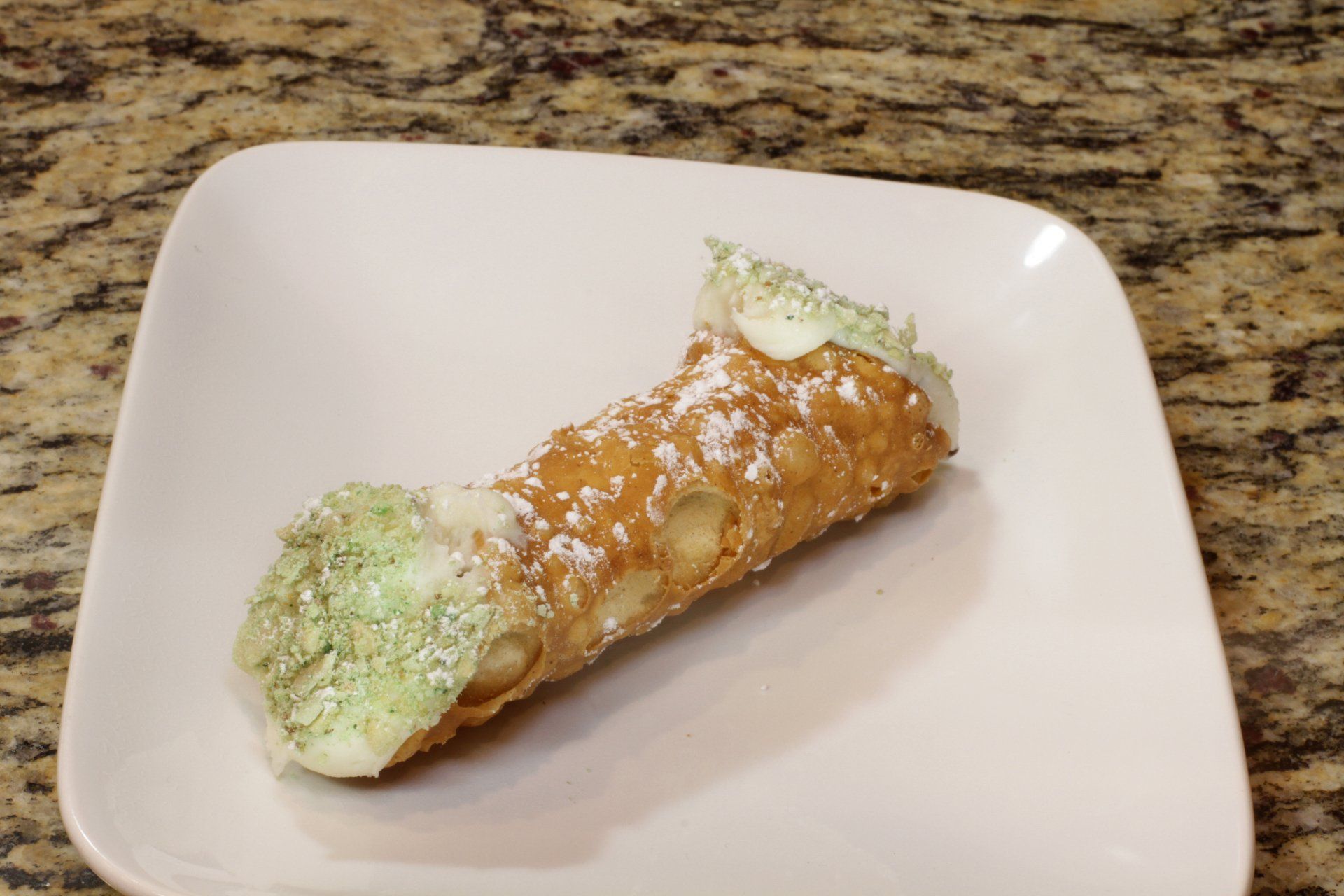 A cannoli on a white plate on a counter.