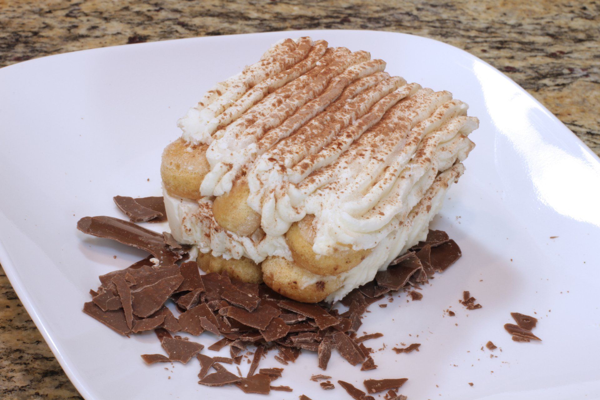 A white plate topped with a piece of cake and chocolate shavings