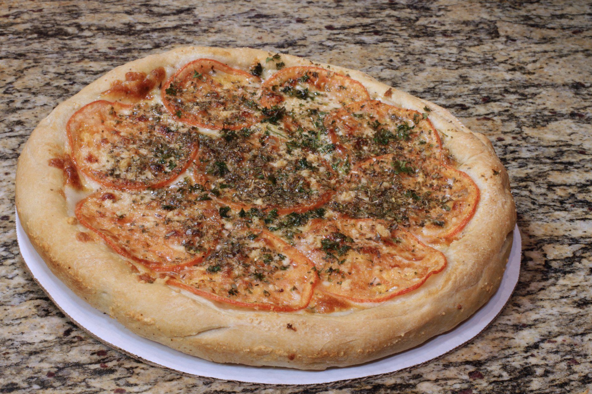 A pizza with tomatoes and cheese on a white plate on a table.
