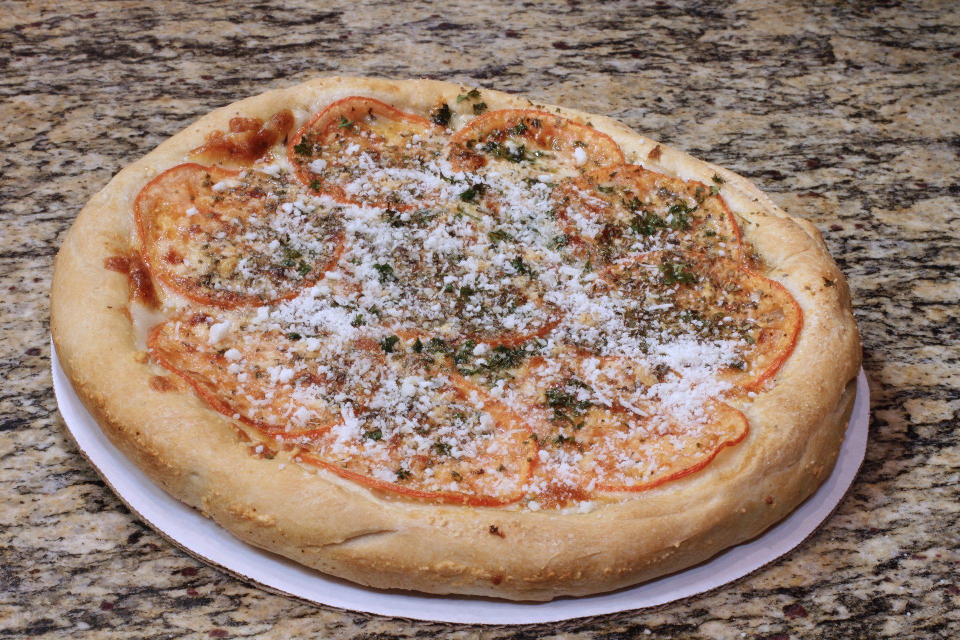 A pizza with tomatoes and cheese is on a paper plate on a table.