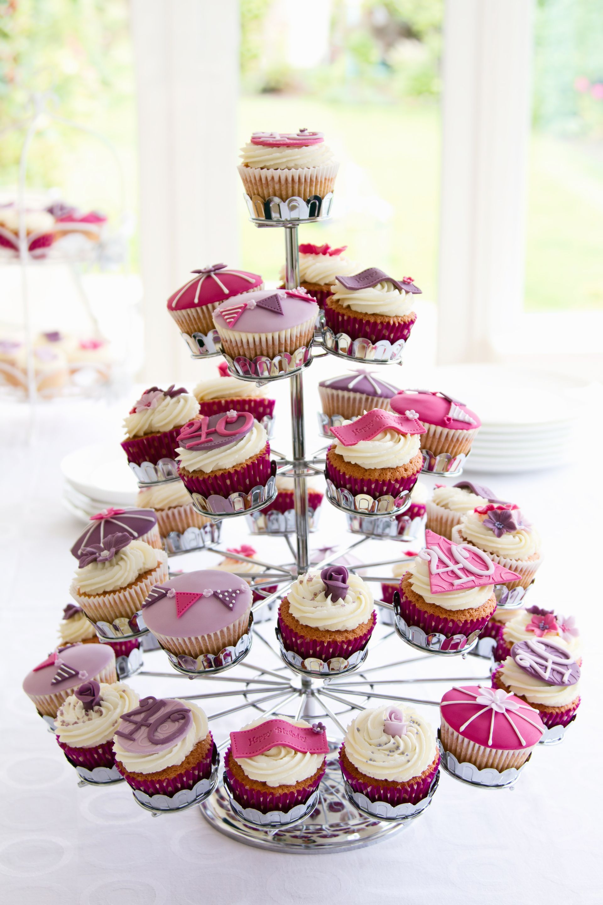 A cupcake stand filled with pink and purple cupcakes on a table.