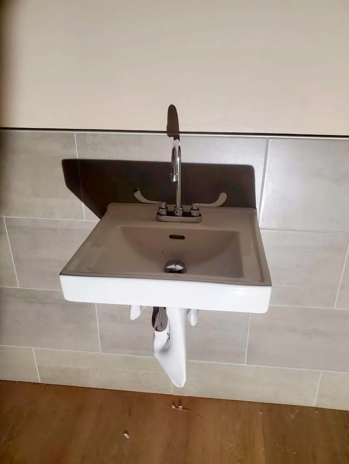 A white sink with a faucet is hanging on a tiled wall.