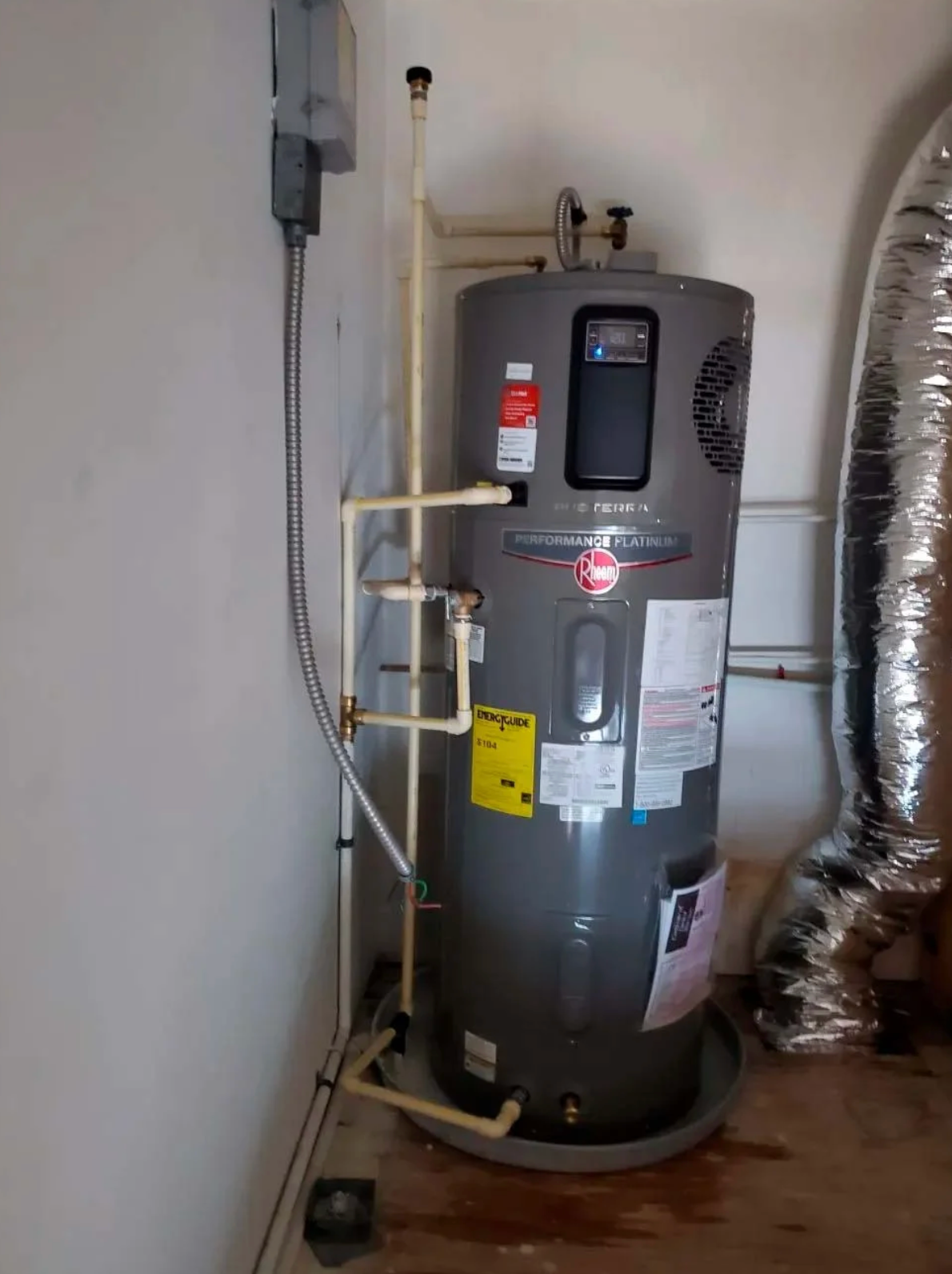 A gray water heater is sitting in a room next to a wall.