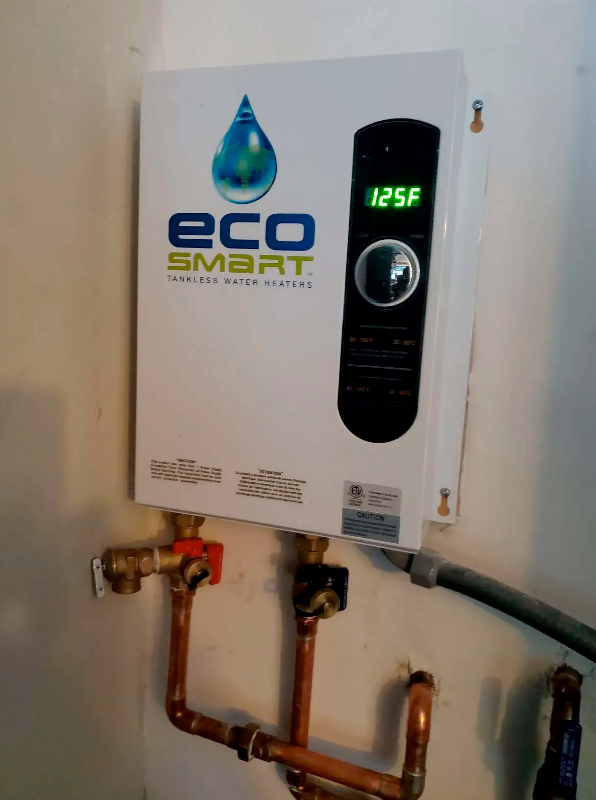 An eco smart water heater is hanging on a wall next to copper pipes.