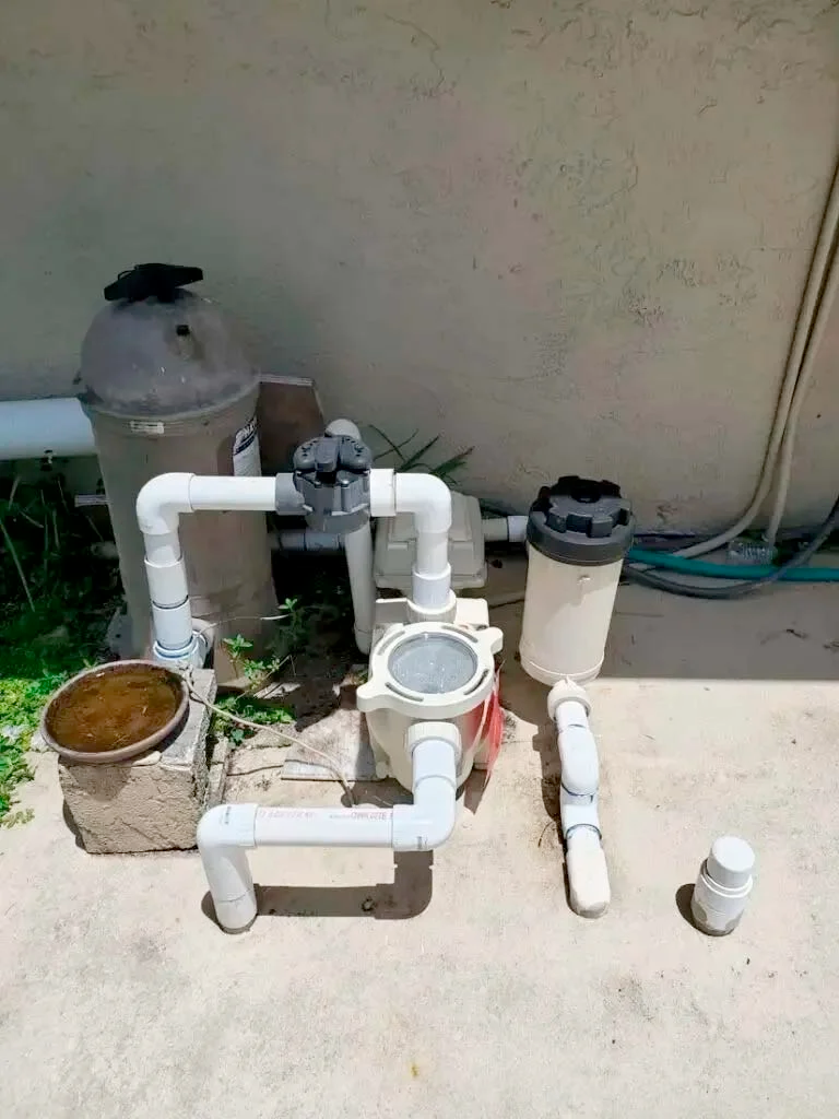 A swimming pool filter is sitting on the ground next to some pipes.