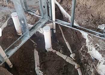 A bunch of pipes are laying in the dirt in a hole.